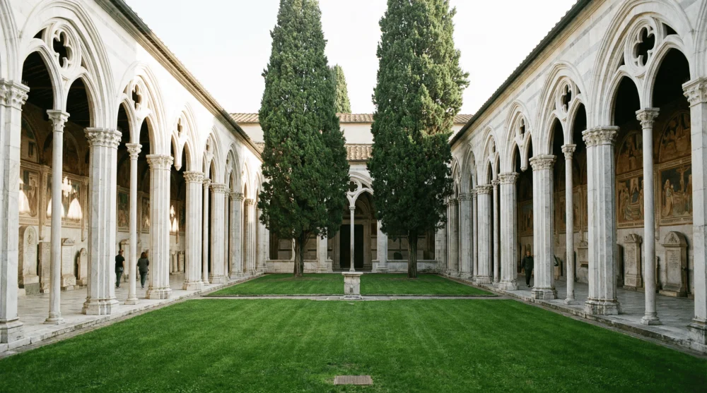 Interior view of Camposanto Monumentale in Pisa featuring white Gothic arches and a green central courtyard