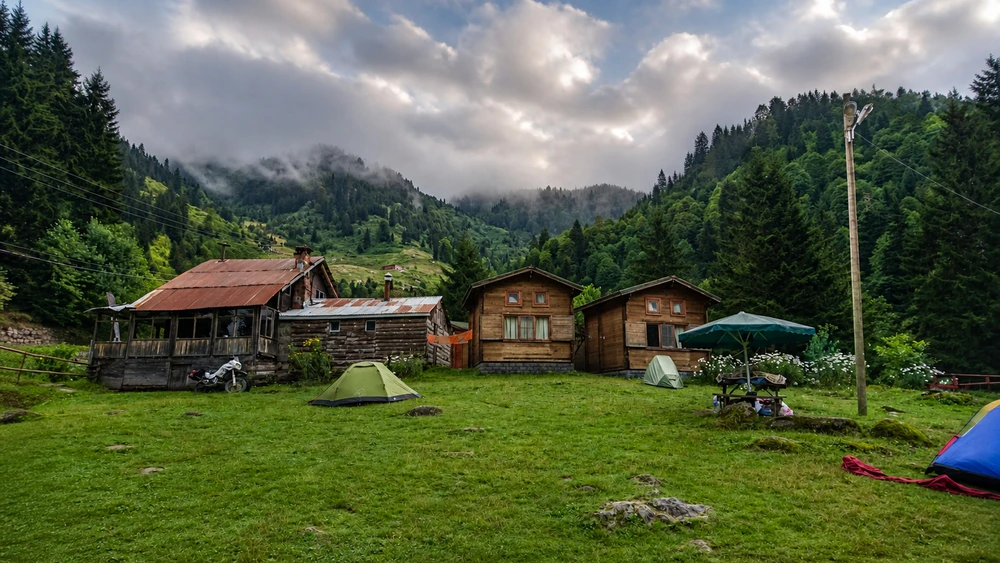Ayder Camping'de ahşap kulübeler ve renkli çadırlar, arka planda dramatik bulutlu gökyüzü