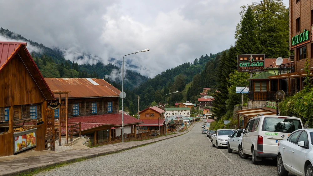 Taş döşeli sokak üzerinde ahşap otel binaları ve park halindeki araçlar