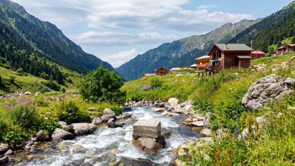 Elevit Yaylası'nda dereden geçen buz gibi su ve arkadaki ahşap evler