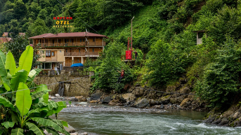 Ahşap otel binası yanındaki zipline platformundan derenin üzerine süzülen ziyaretçi