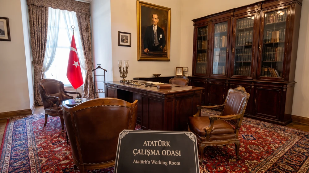 Atatürk'ün çalışma odasında koyu ahşap masa, deri koltuklar, Türk bayrağı ve cam kapaklı kitaplık