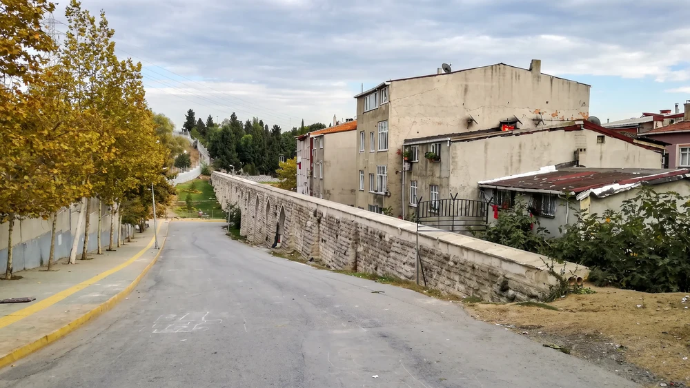 Yol kenarında uzanan taş su kemeri duvarı ve yanındaki apartmanlar