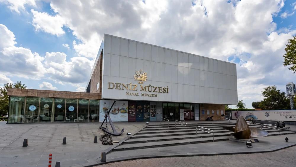 Deniz Müzesi'nin cam ve taş cepheli giriş binası, önünde demir çapa ve merdivenler.