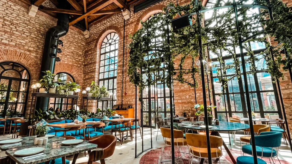 Yüksek kemerli pencereleri ve tuğla duvarları olan, bitkilerle donatılmış iç mekan