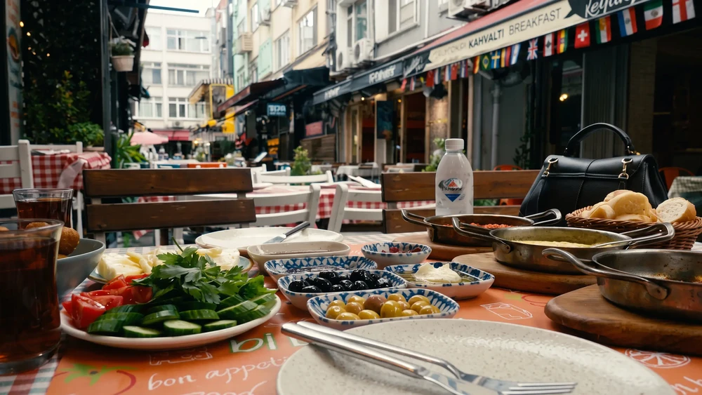 Açık havada kahvaltı sofrası: peynir, zeytin, domates, salatalık ve çay bardakları