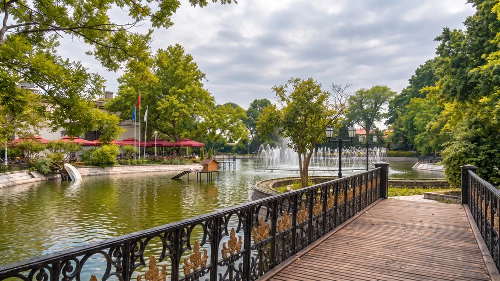 Yıldız Parkı'ndaki gölün kıyısında fıskiyeler, ahşap iskele ve kırmızı şemsiyeli kafe alanı